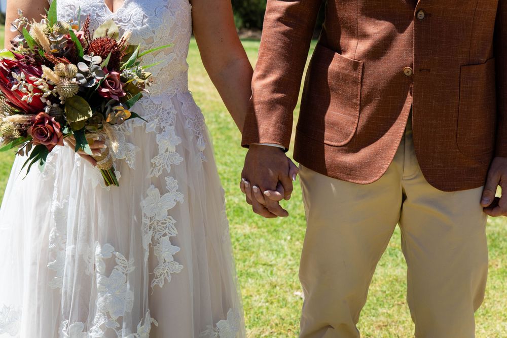 Close up of couple holding hands with vibrant wedding bouquet.