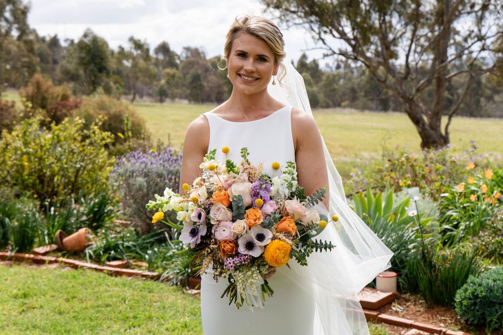 Bride holds colorful wildflower bouquet in garden setting.