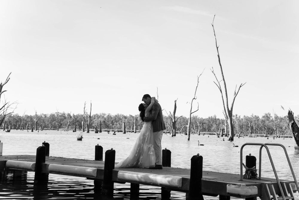 Dramatic black and white wedding photo on wooden dock over lake.
