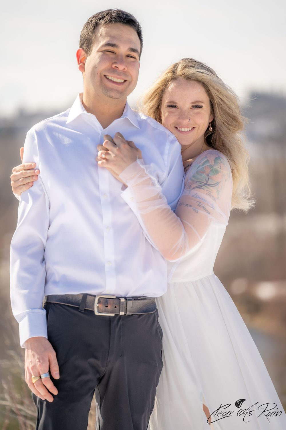 Couple in white and pink formal attire embracing outdoors on a sunny day.