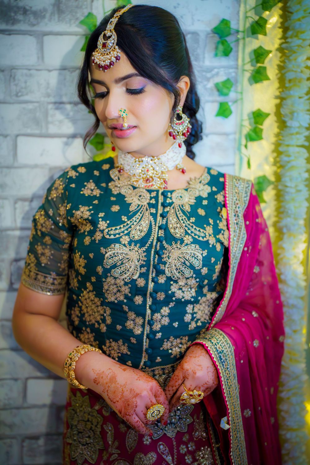 Traditional bridal attire featuring an embroidered teal blouse with gold details, pink dupatta, and ornate jewelry.