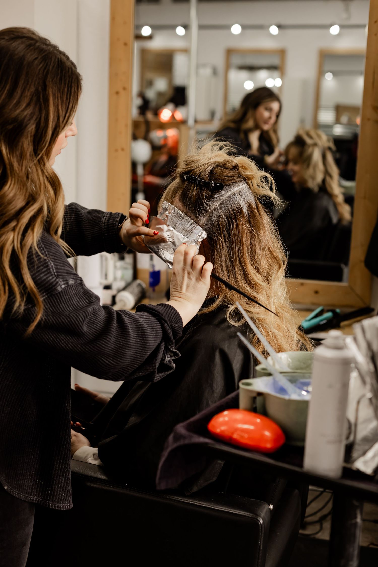 A salon stylist foiling a client's hair in her salon chair for her social media branding session with a moody vibe.