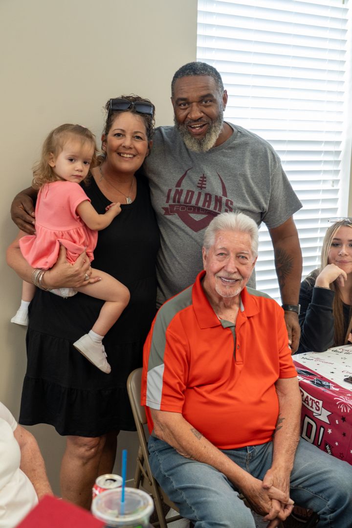 Multi-generational family gathering in a home interior with a small child in a pink dress.