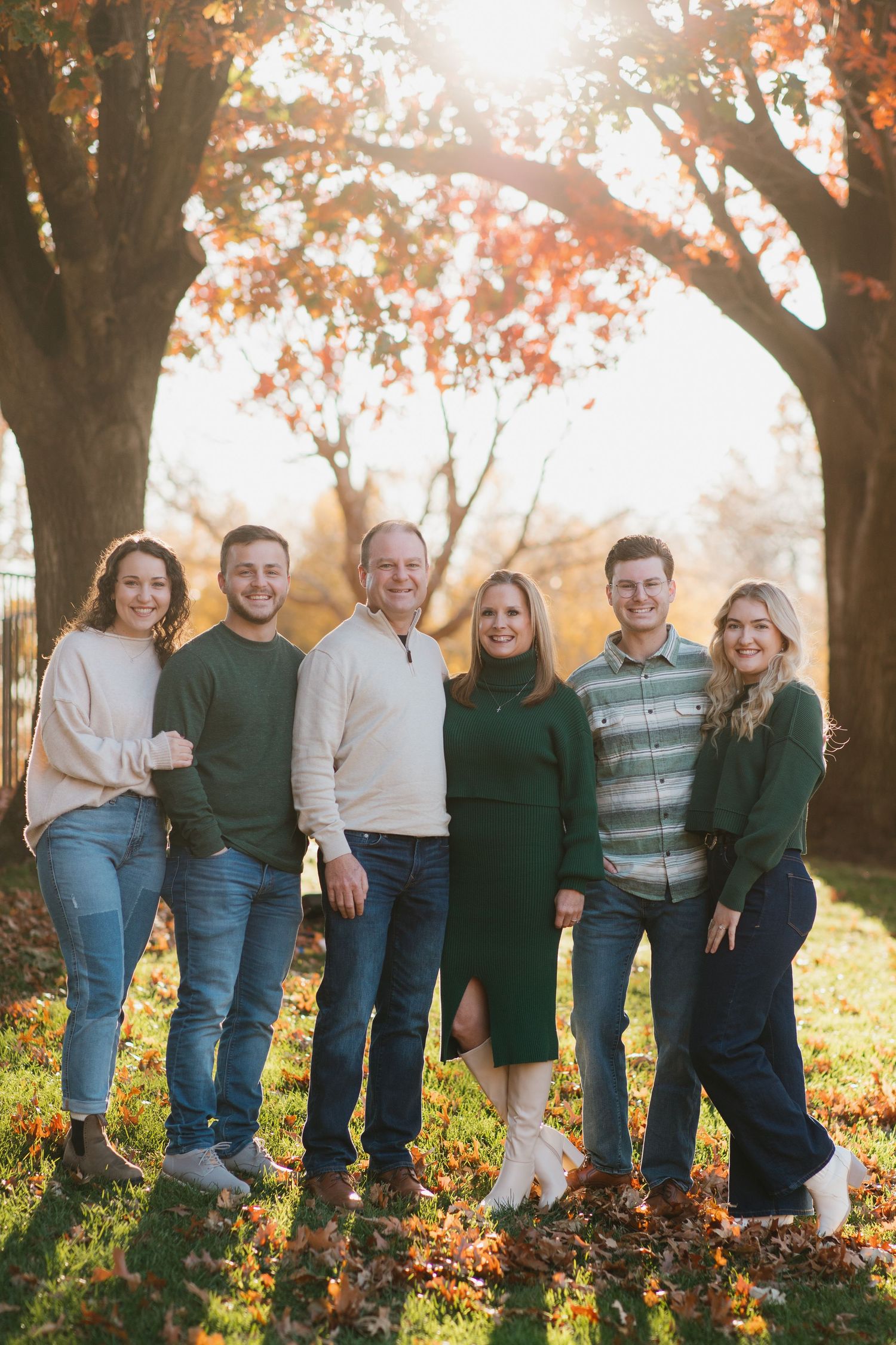 Oklahoma Family group in coordinated green and beige outfits poses among autumn trees.