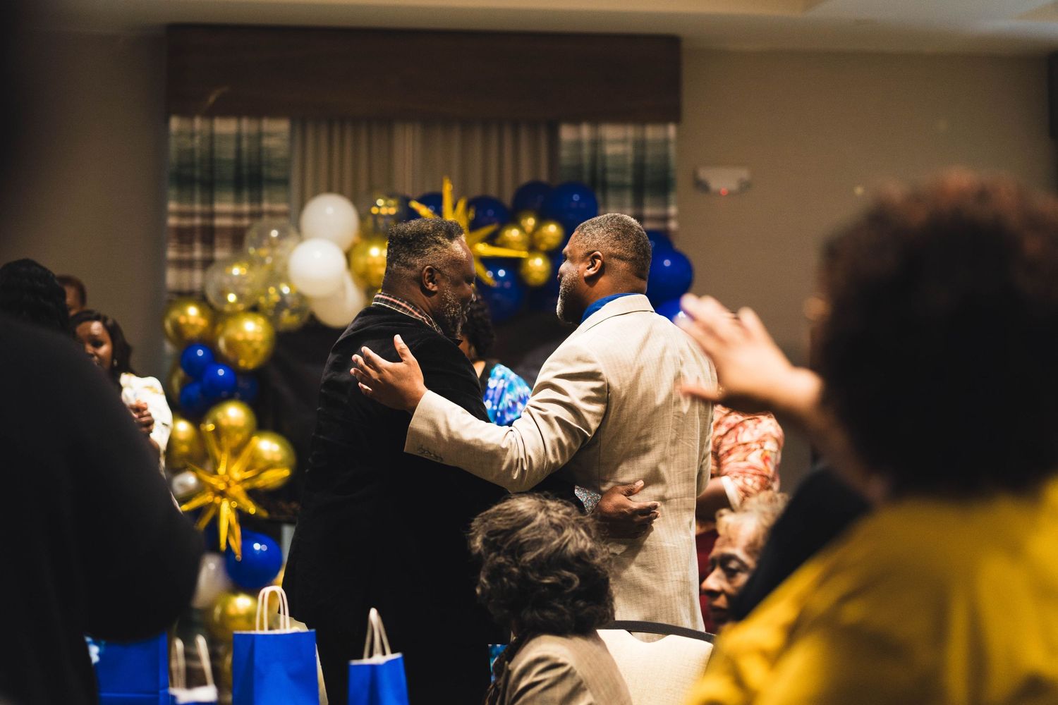 A celebratory gathering with blue and gold balloons decorating an indoor event space.