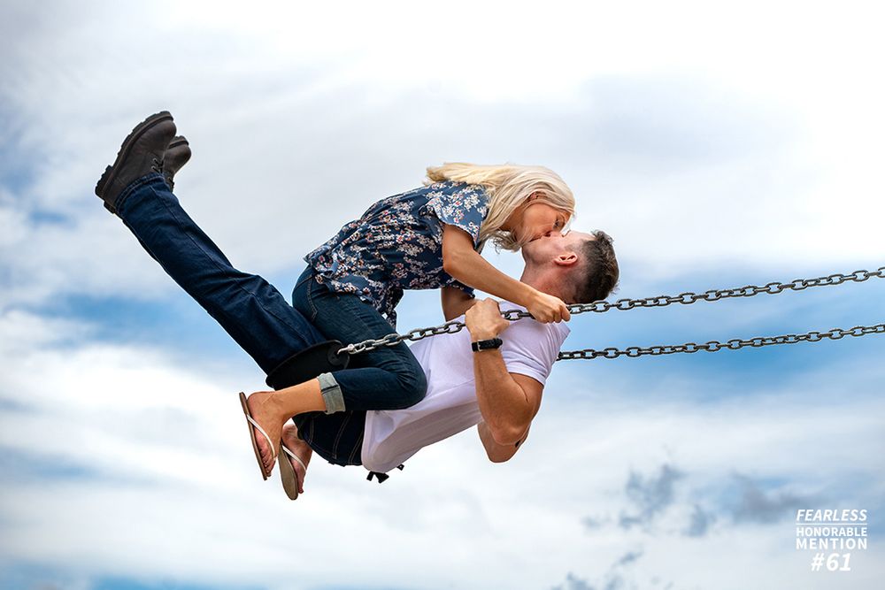 Playful couple swinging together against a cloudy sky.