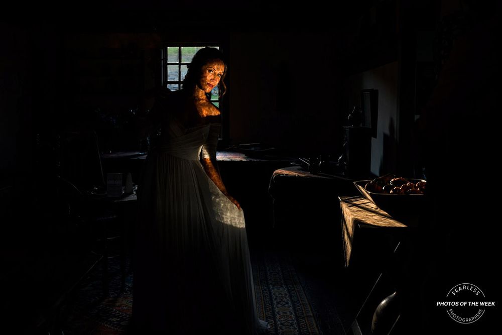 Dramatic low-light portrait in a rustic interior with window lighting.