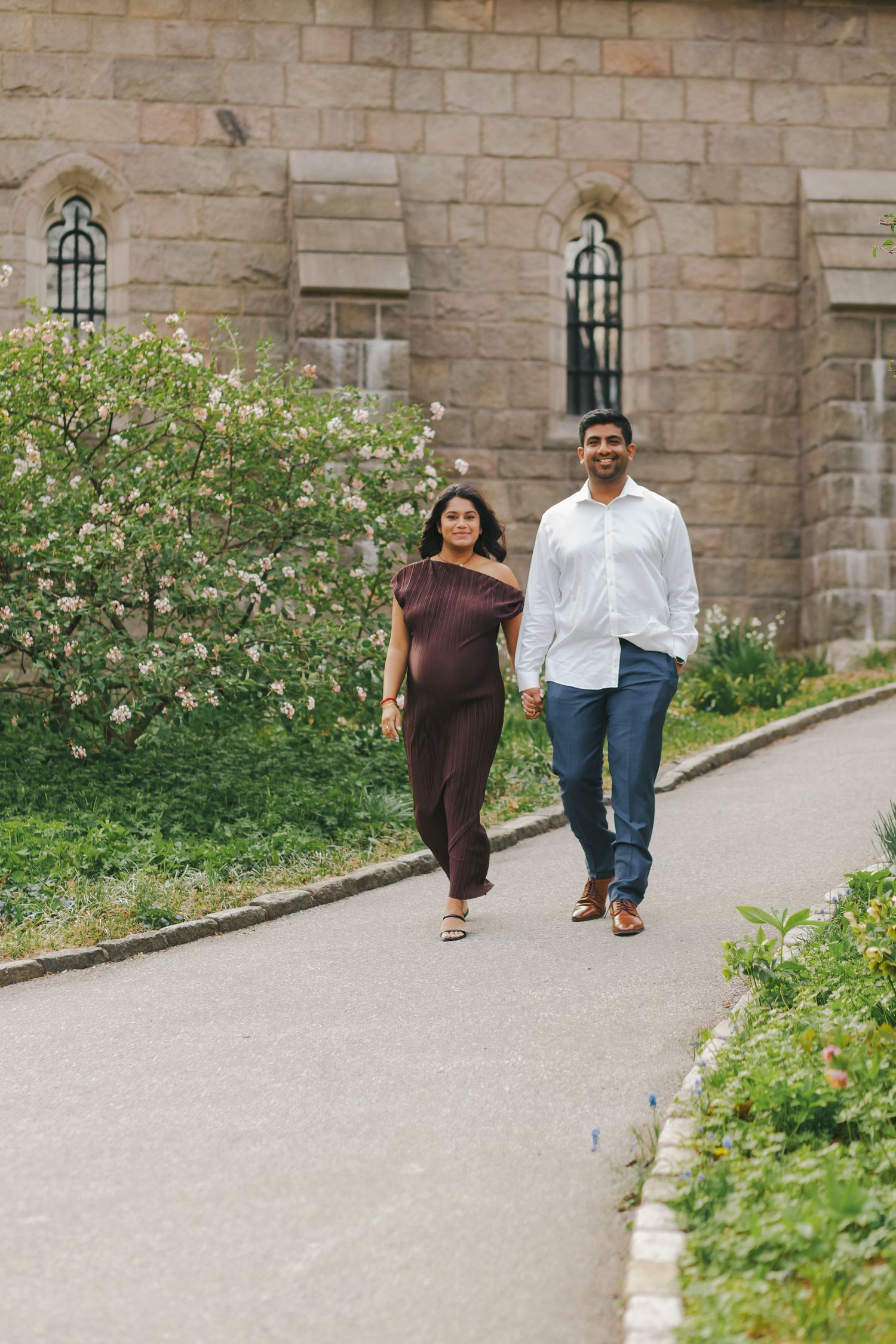 Couple walking through Fort Tryon Park with the historic castle in the background, beautifully captured at golden hour.