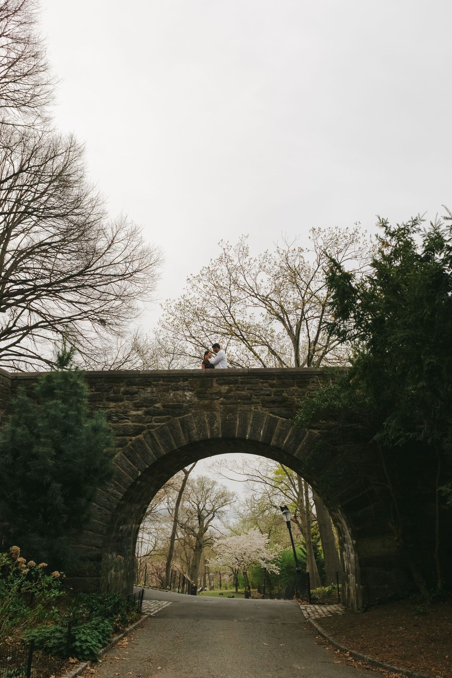 Artistic silhouette of couple standing on the bridge, framed by golden-hour light, by NYC maternity photographer Paula Brearley.