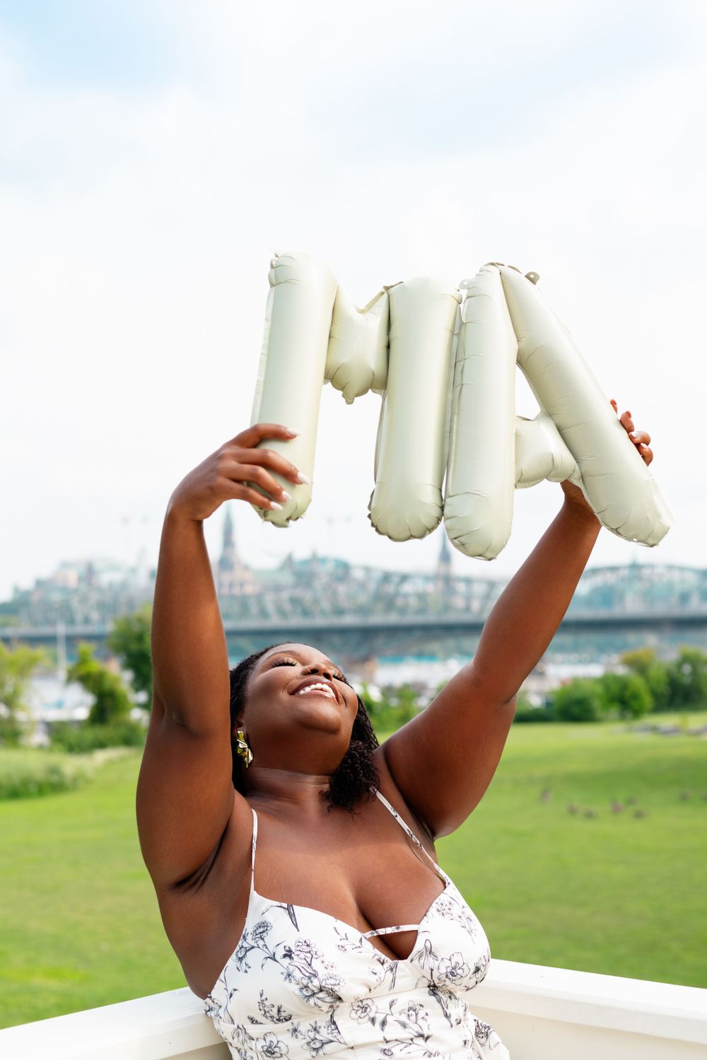 Joyful moment captured holding inflatable letters against blue sky and bridge background.