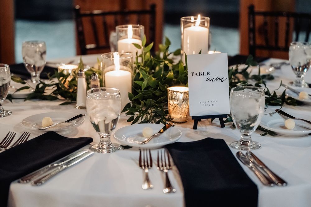 Elegant wedding table setting with white candles, greenery centerpiece, navy napkins and crystal glassware.