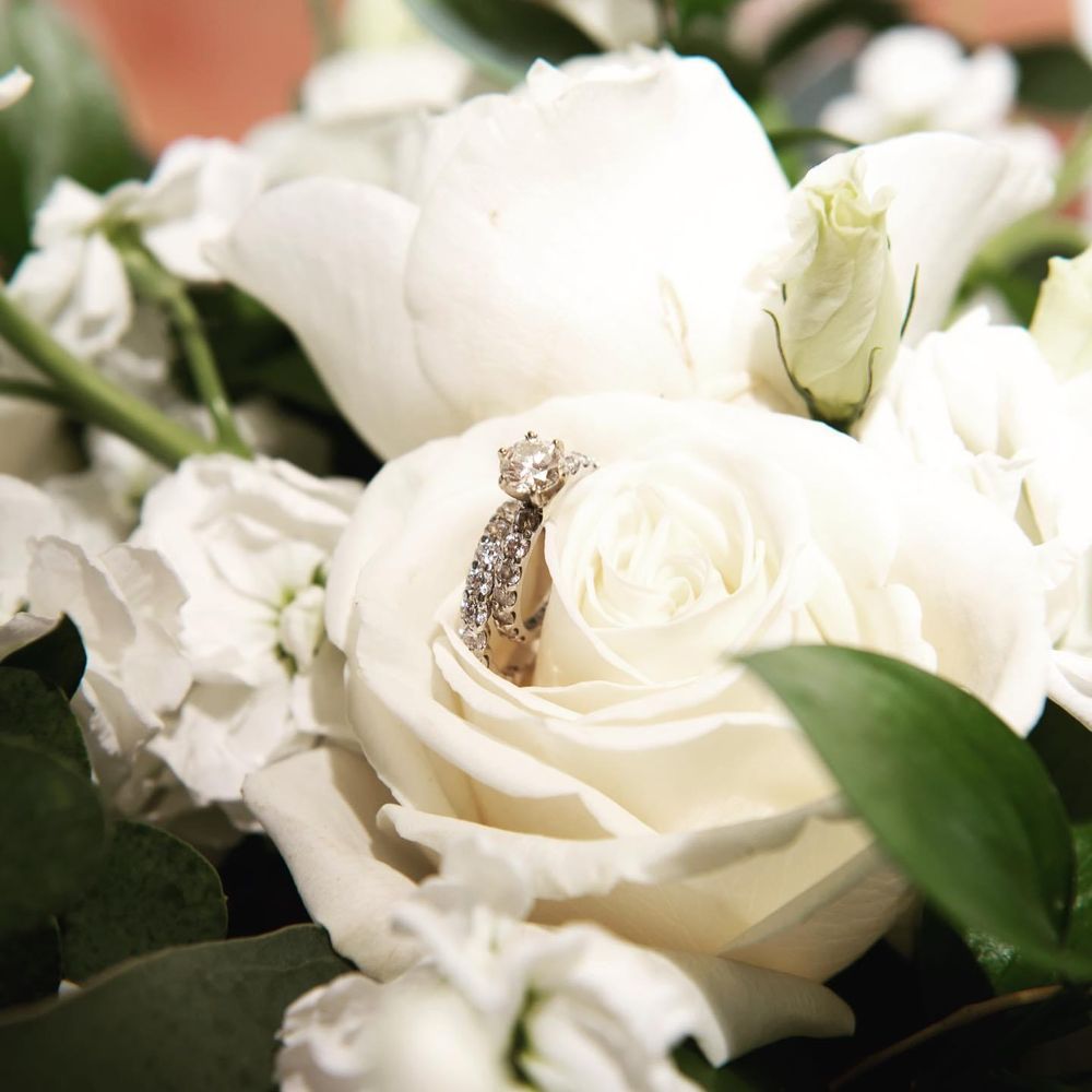 Diamond engagement ring nestled among white roses and greenery.