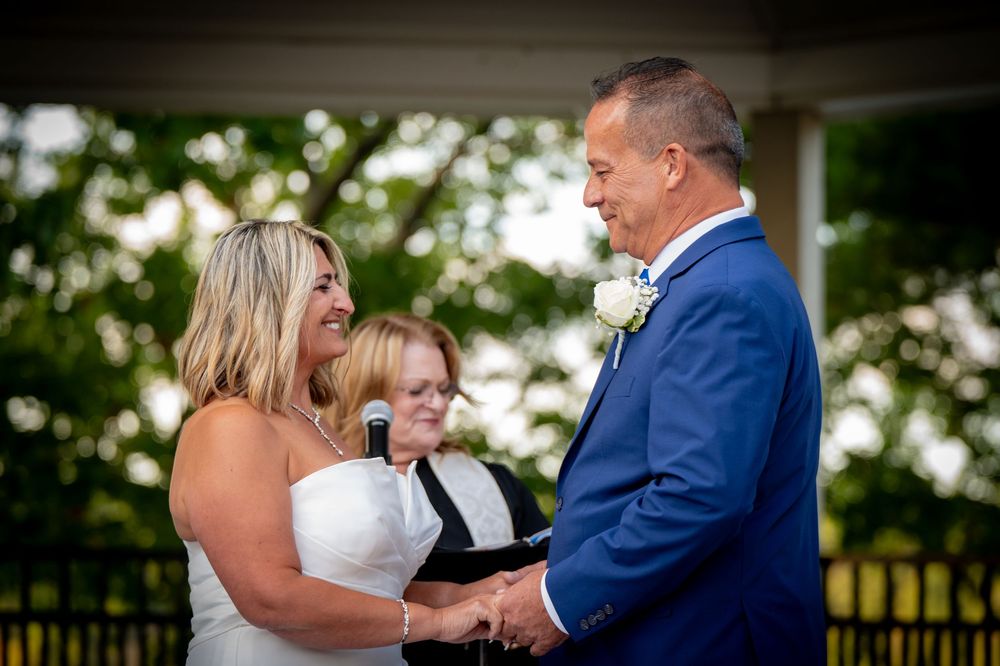 A couple holds hands during an intimate outdoor wedding ceremony on a sunny afternoon as a young ring bearer looks on.