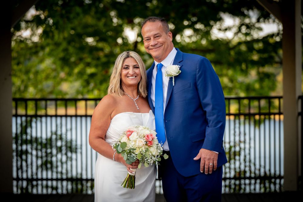 A couple in wedding attire poses together outdoors, with the bride holding a peach and white floral bouquet.