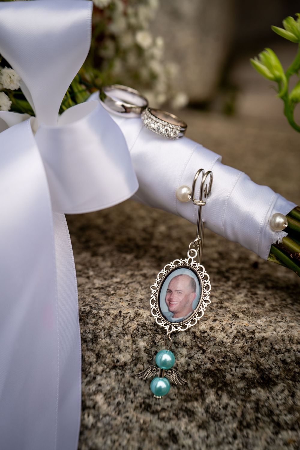 Wedding bouquet with white ribbon bow and wedding rings next to a memorial charm with turquoise beaded accents.