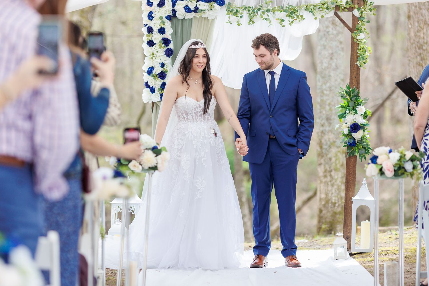 Newlyweds walking down aisle under floral arch with photographers capturing the moment.