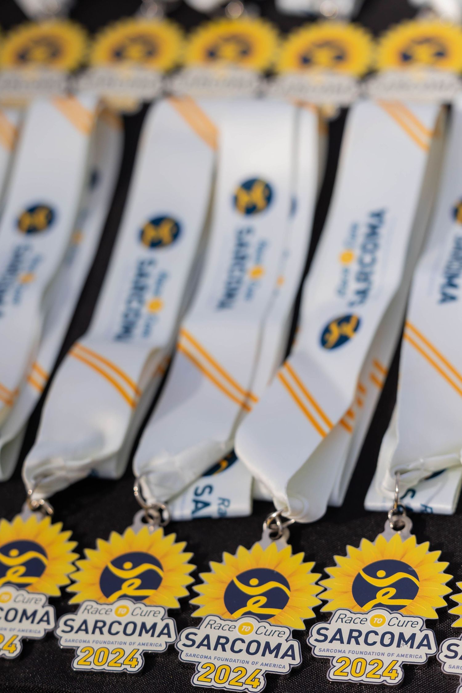 Row of white and gold Sarcoma 2024 race medals with yellow sunflower designs displayed.