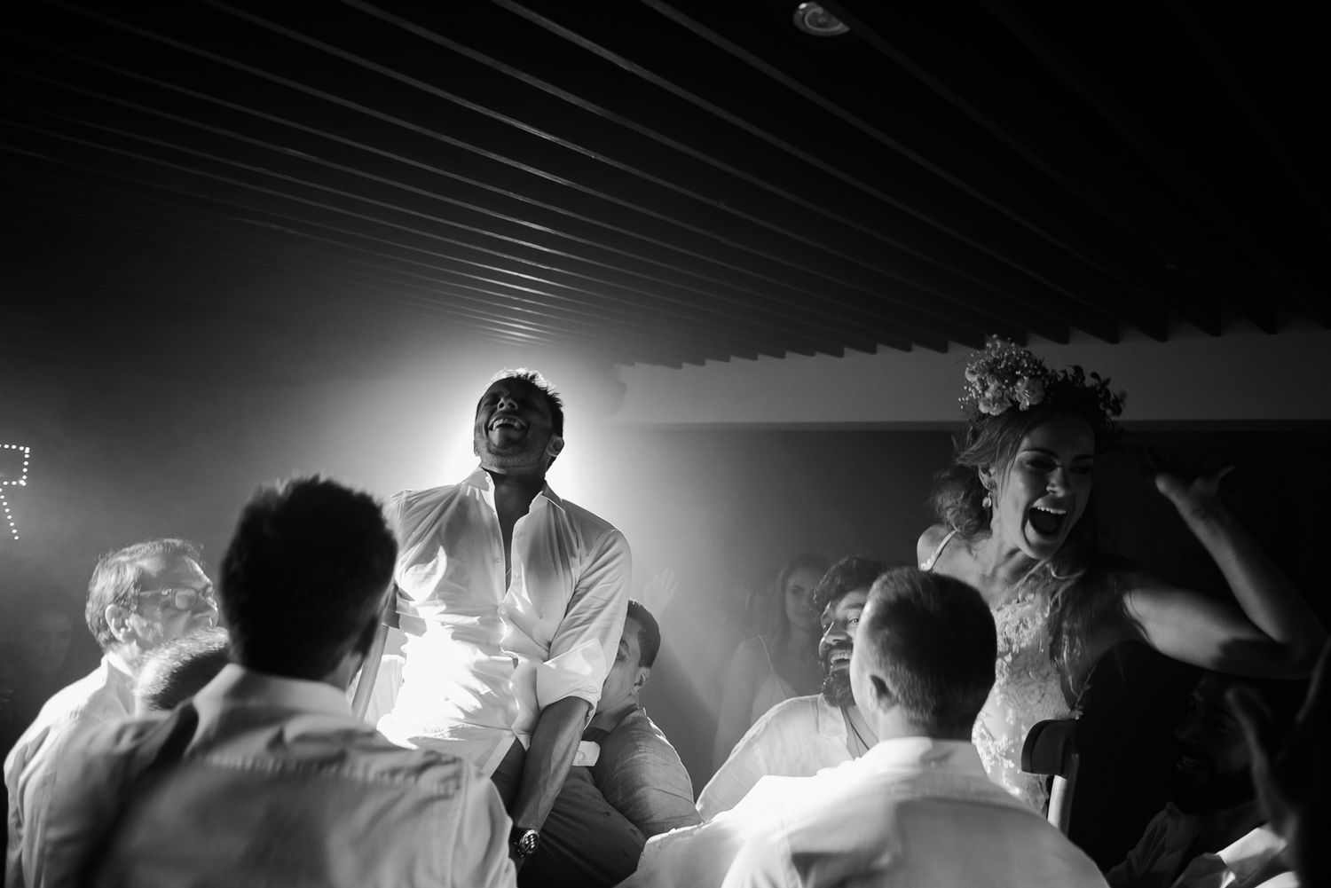 A group of people dancing and celebrating energetically at a party with dramatic lighting effects in black and white.