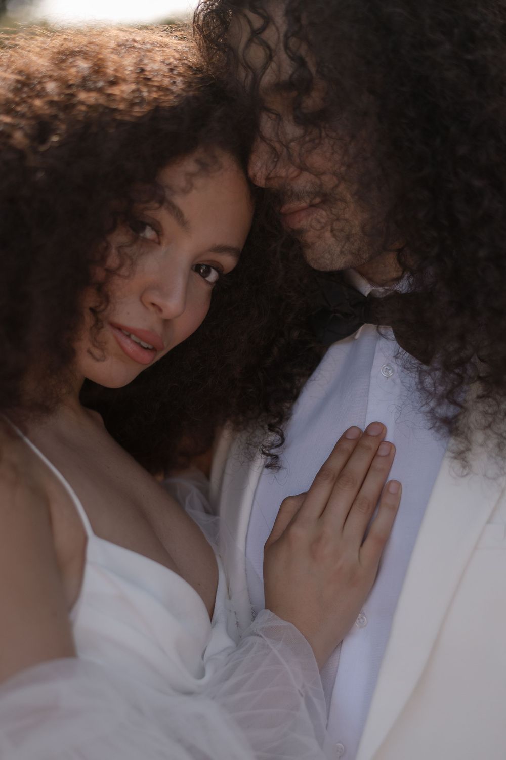 A romantic bridal portrait featuring white wedding attire and natural curly hair in soft lighting.