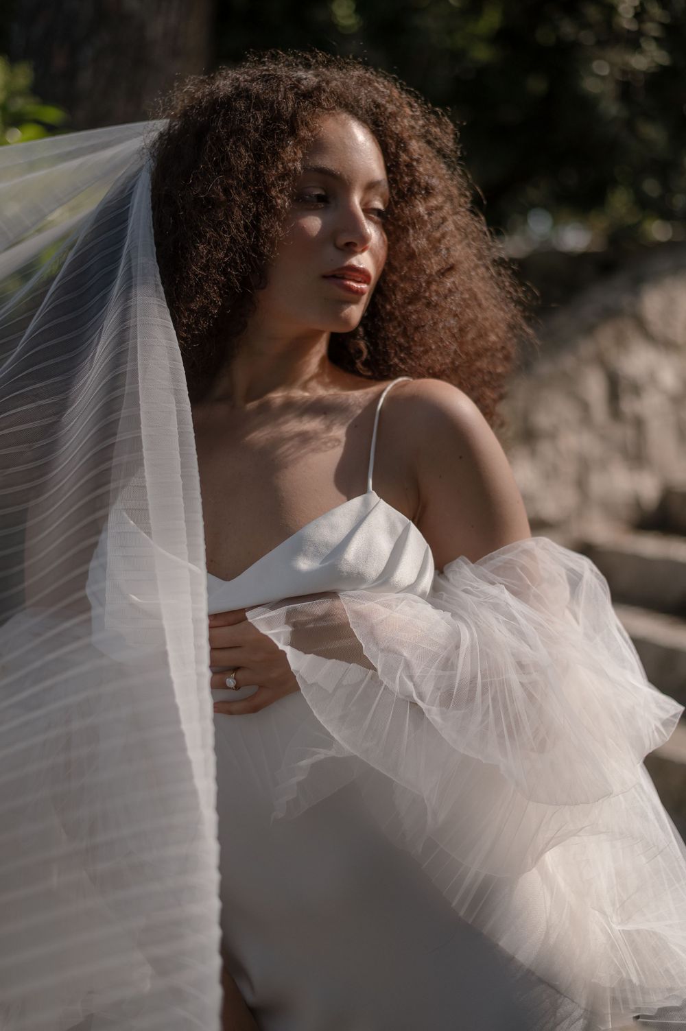 A bride in a white wedding dress with voluminous tulle sleeves poses in romantic natural lighting outdoors.