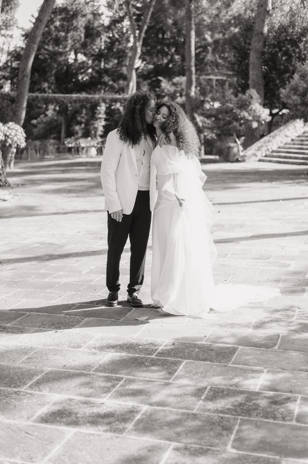 A black and white photo of a wedding couple sharing an intimate moment on stone pavement.