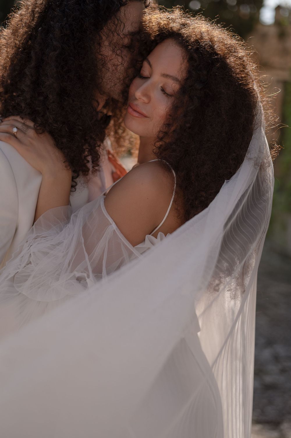 Ethereal portrait of a person in flowy white fabric with natural curly hair backlit in golden sunlight.