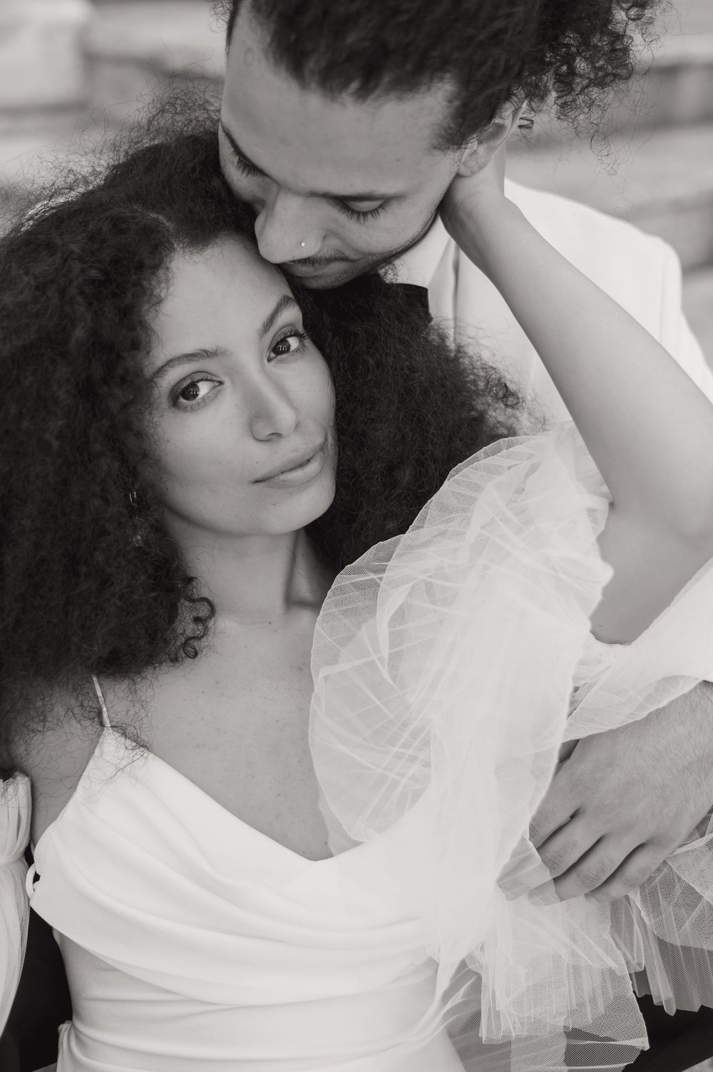 Intimate black and white portrait of couple embracing in formal white attire.
