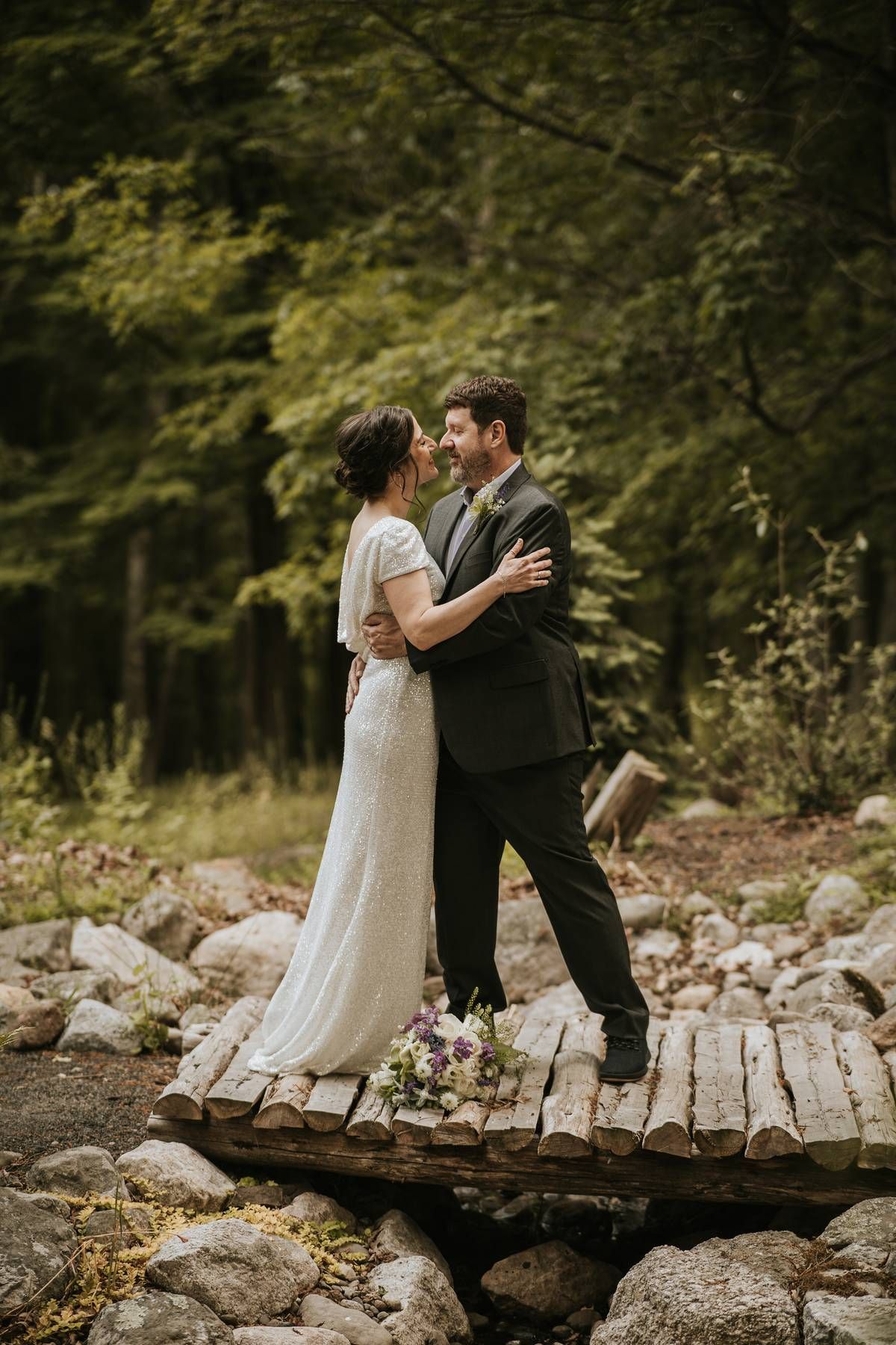 a couple holding each other about to kiss on a small bridge in the woods on their wedding day