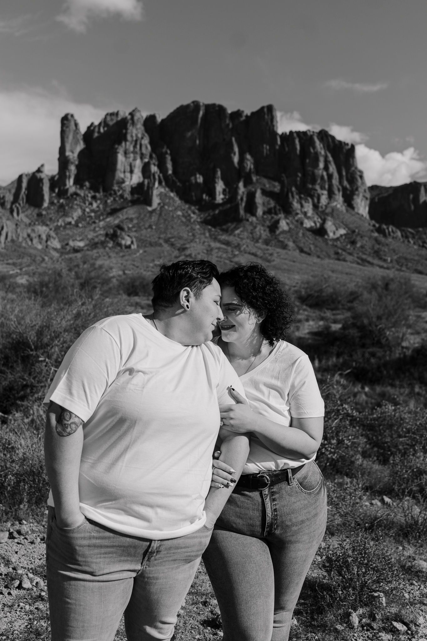 A couple shares a tender moment against a dramatic desert mountain backdrop in black and white.