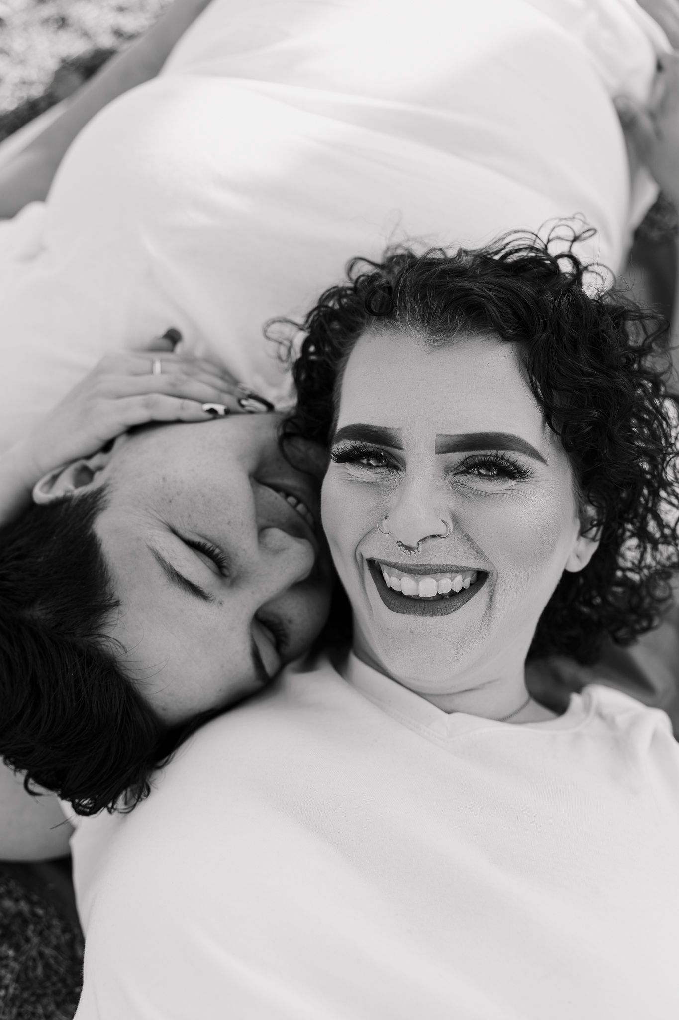 A joyful black and white close-up of two individuals lying together and smiling.