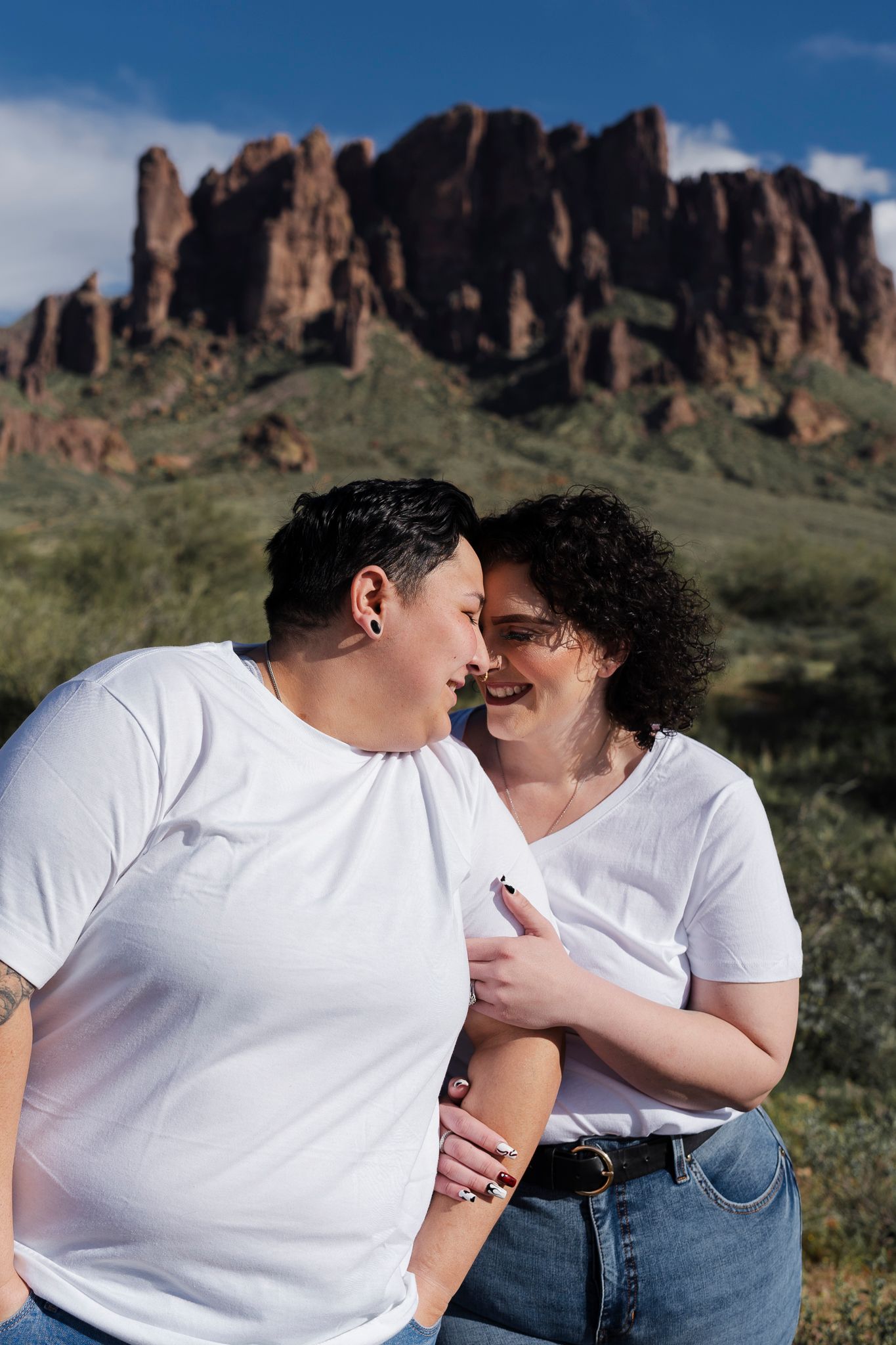 A couple in matching white shirts embraces while standing in front of rugged desert cliffs.