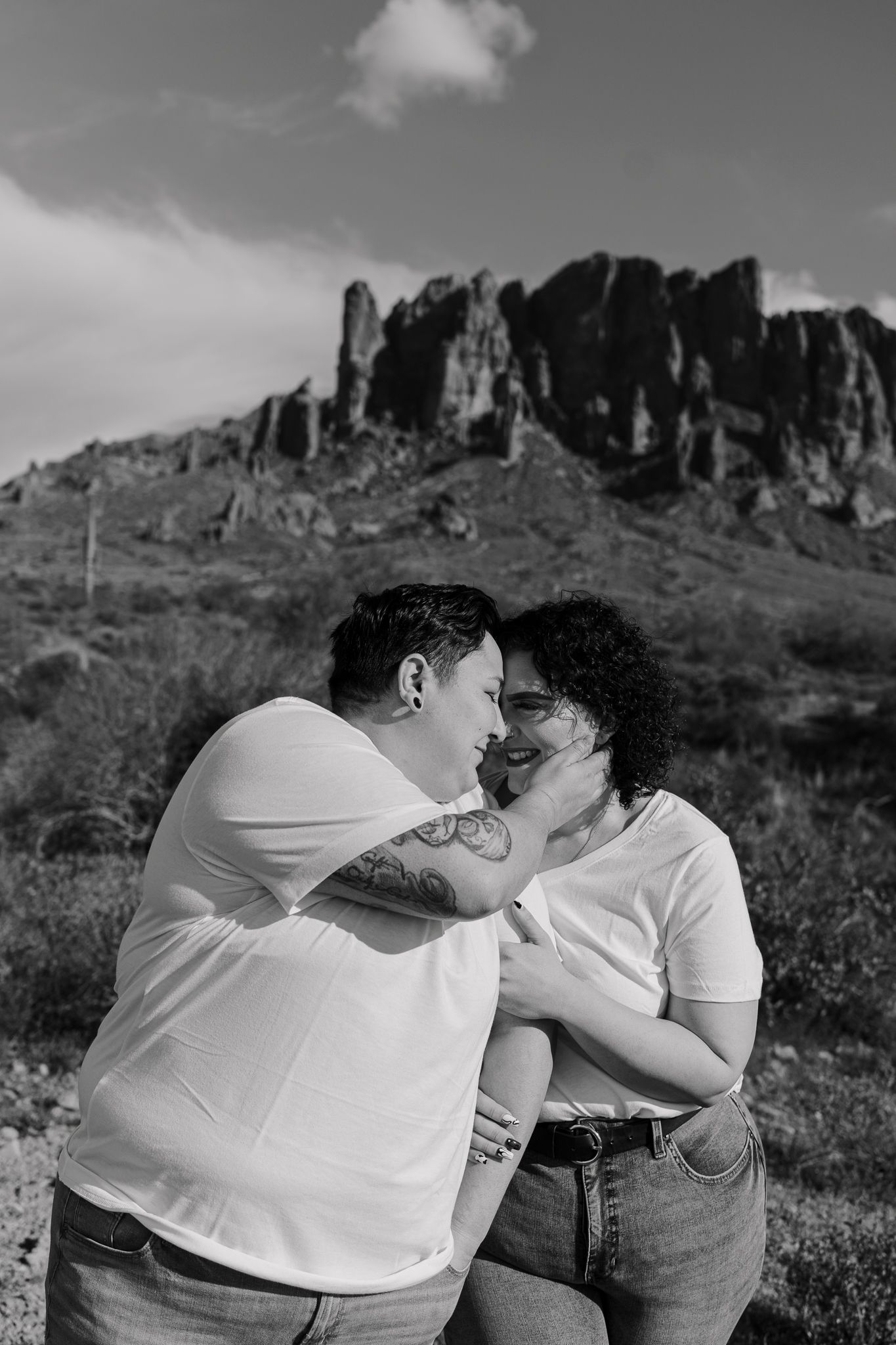 A loving black and white portrait of a couple with mountainous desert scenery behind them.