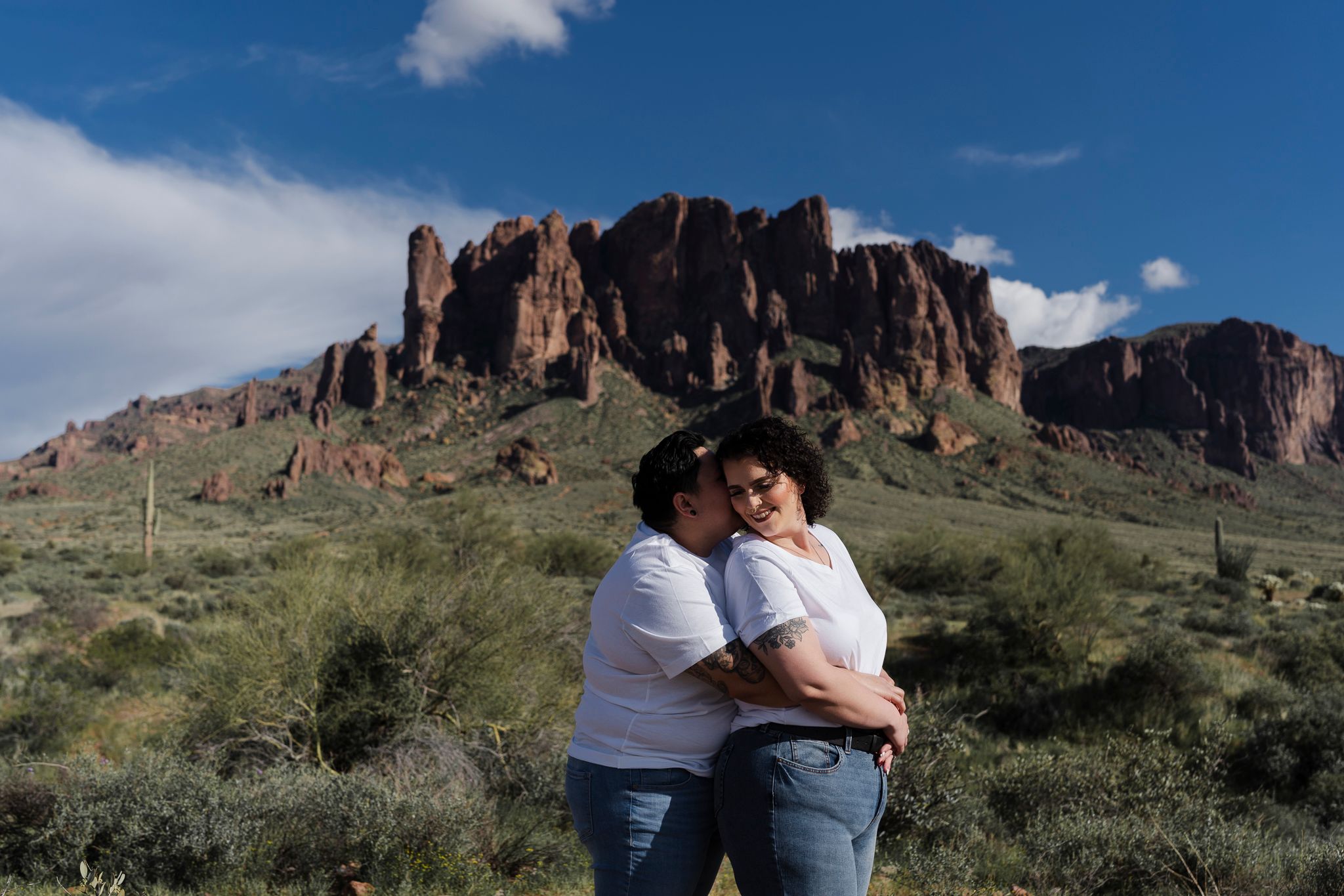 A couple embraces in an intimate moment with dramatic desert rock formations in the background.