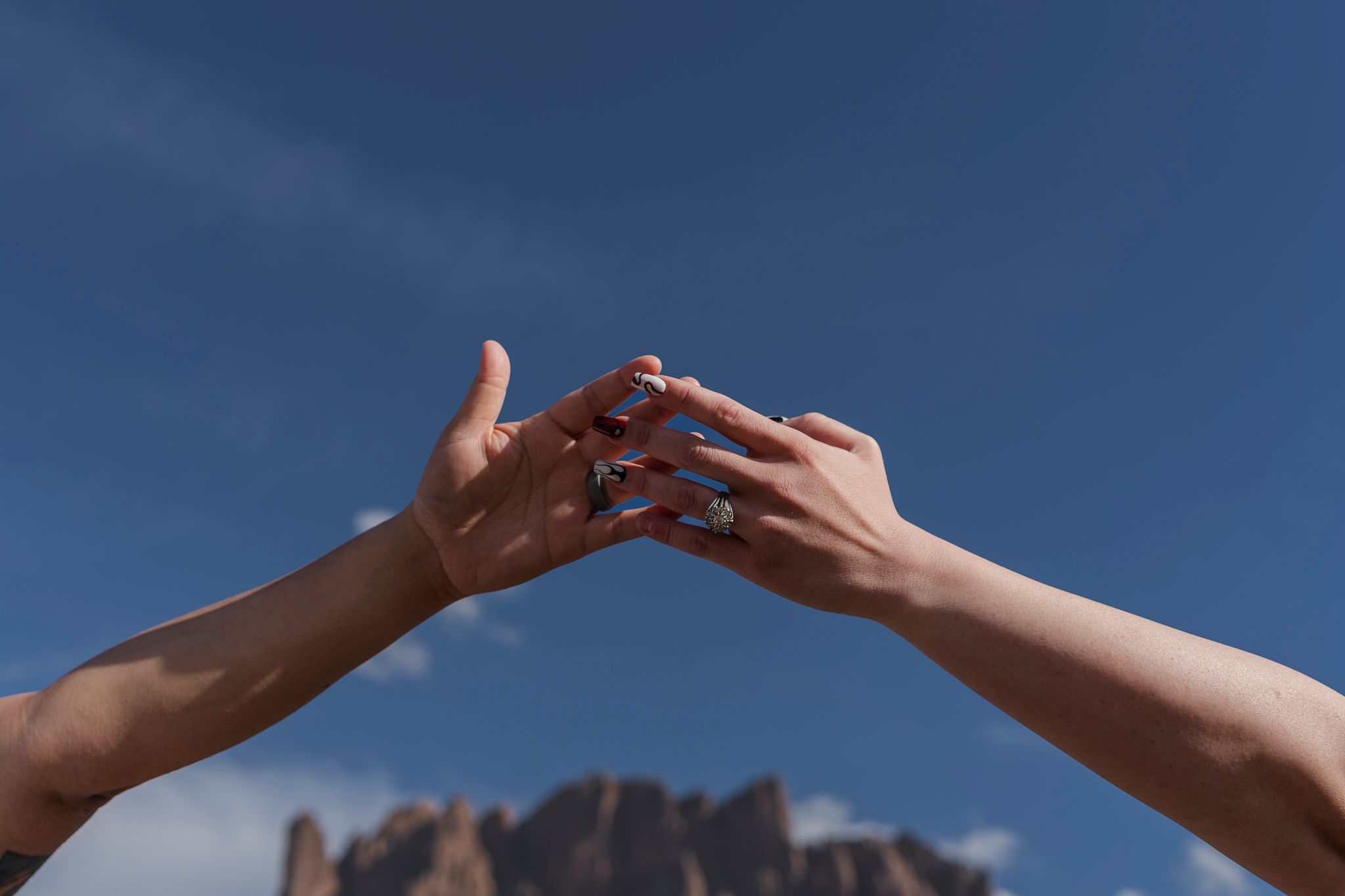 Two hands reach toward each other against a blue sky with desert mountains in the background.