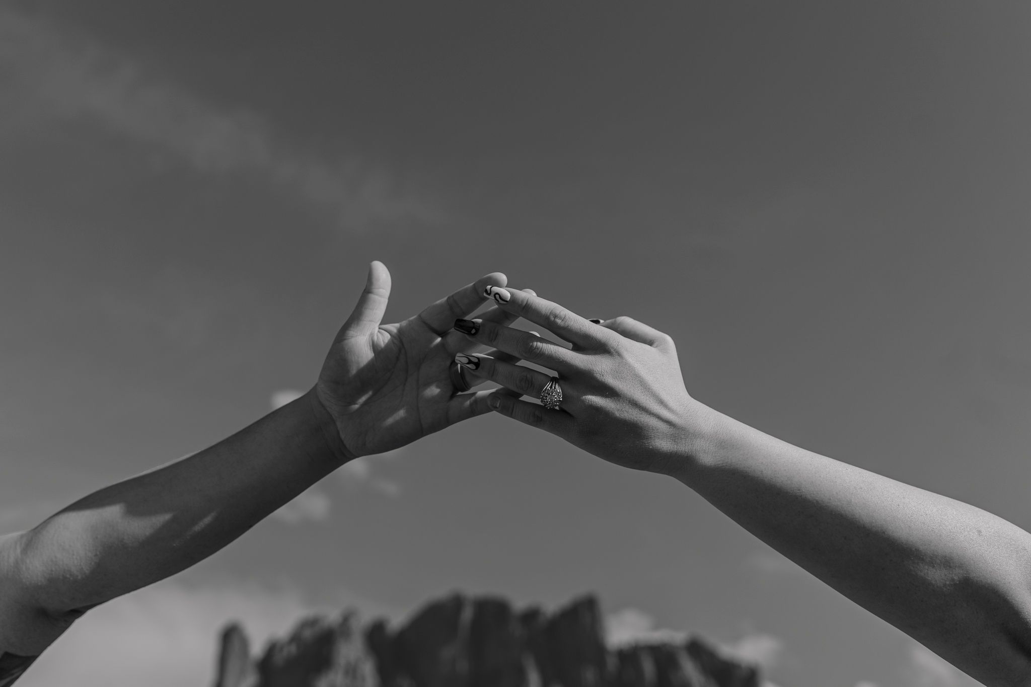 A black and white photo of hands reaching toward each other with mountain silhouettes.