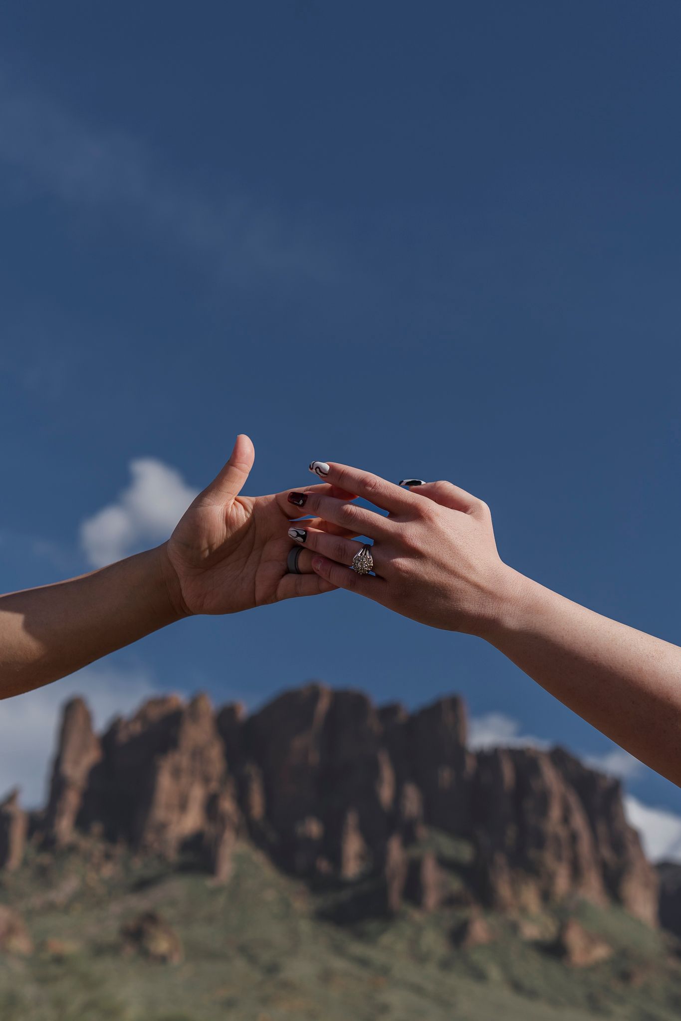 Hands touching tenderly in front of desert mountain landscape under blue sky.
