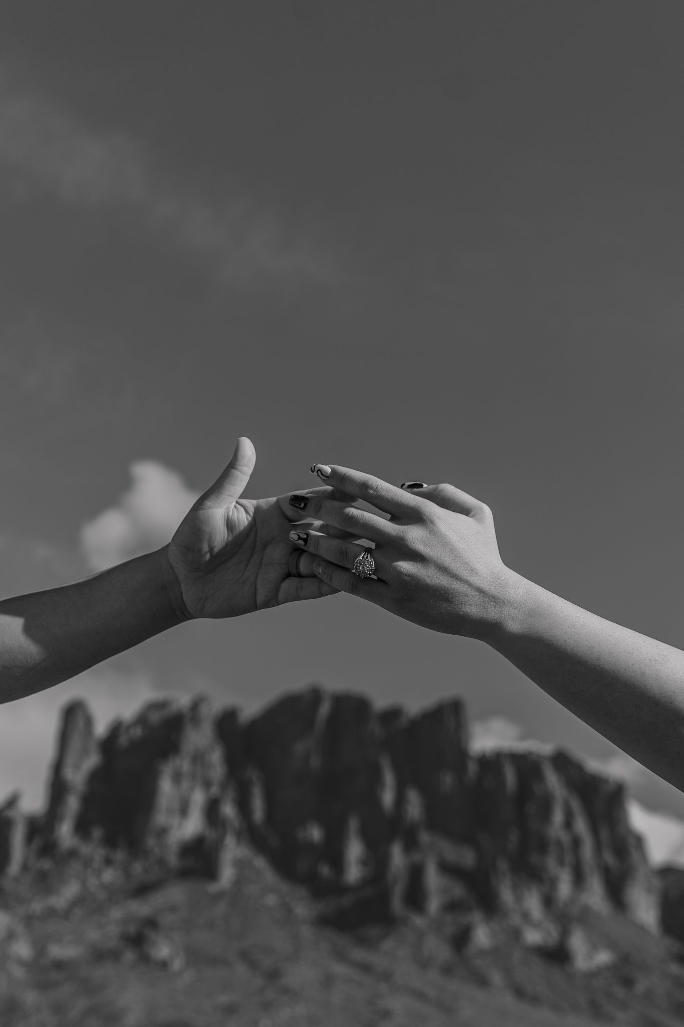 Artistic black and white capture of hands meeting with desert cliffs in background.
