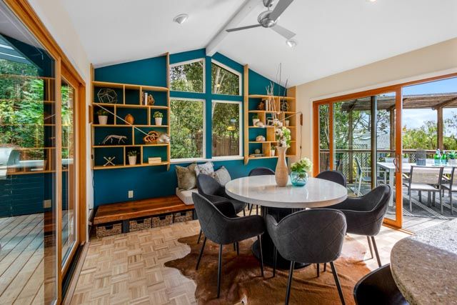 Modern dining room with teal walls, built-in shelving, and large windows overlooking nature.