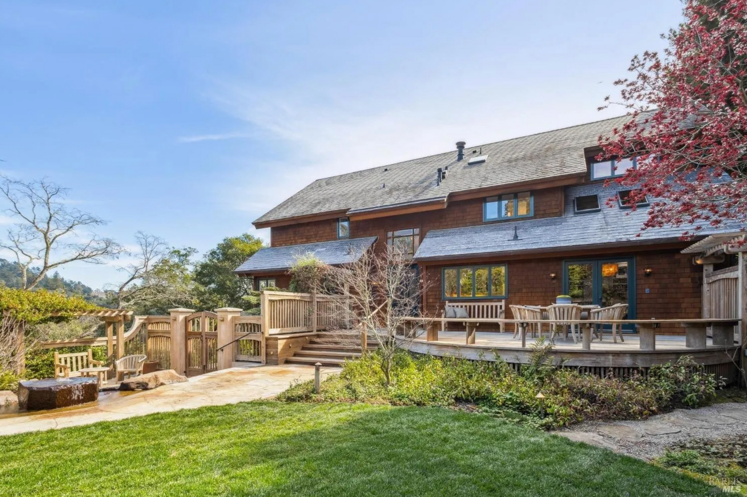 Large rustic timber house with wooden deck and landscaped lawn garden on sunny day with blue sky background.