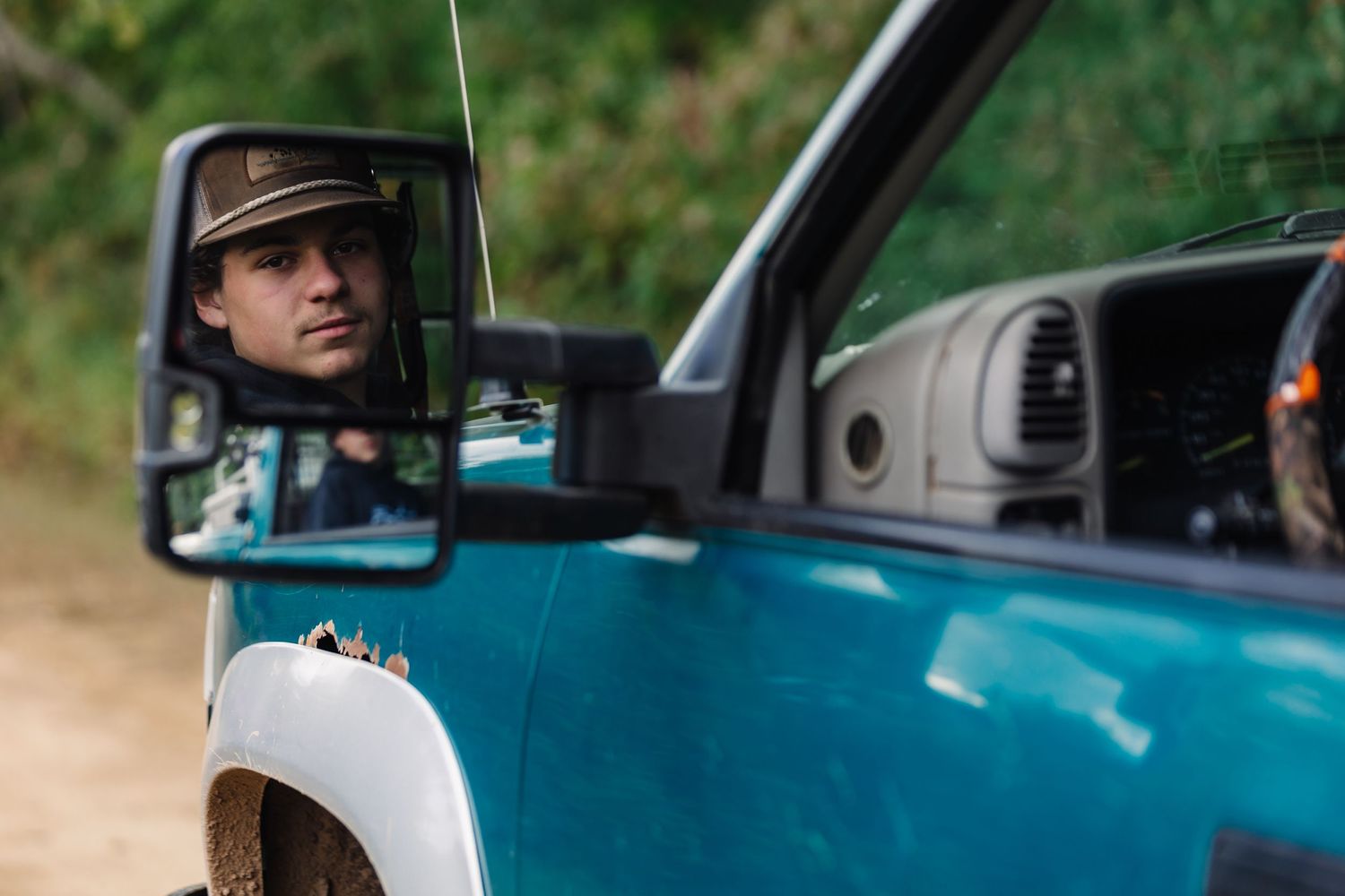 Side view mirror reflection of blue pickup truck parked in green surroundings.