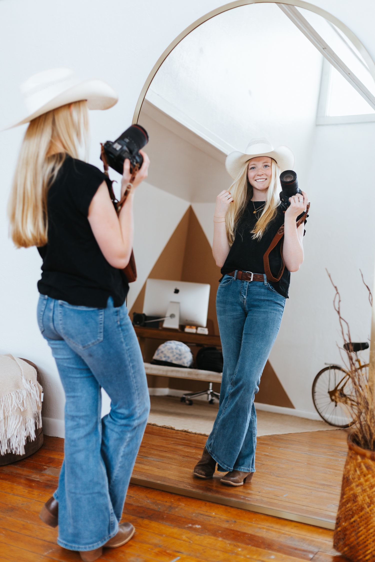 A reflection in a mirror shows someone taking photos while wearing a cowboy hat and denim.