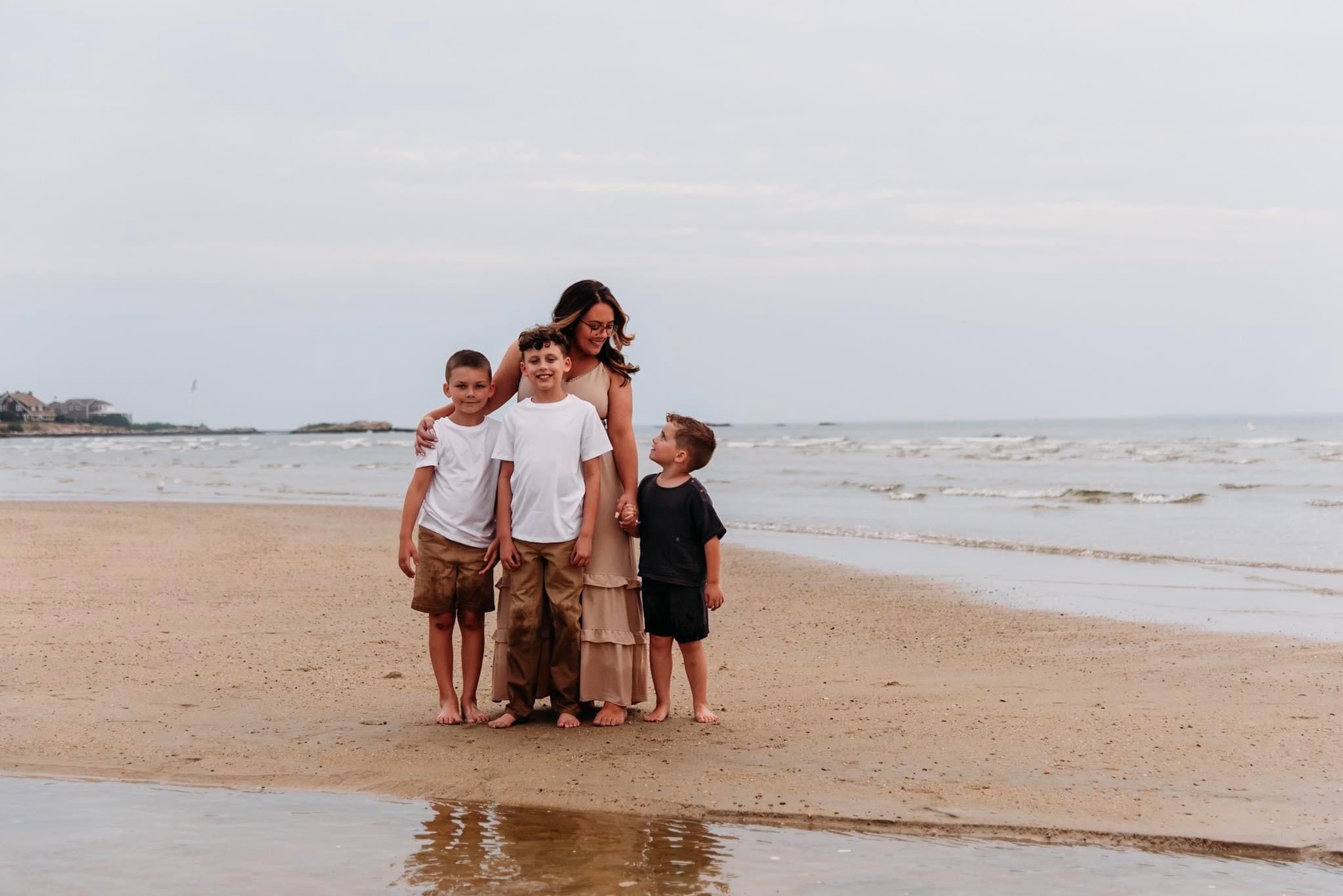 Family group standing together on a sandy beach at the ocean shore during overcast weather.