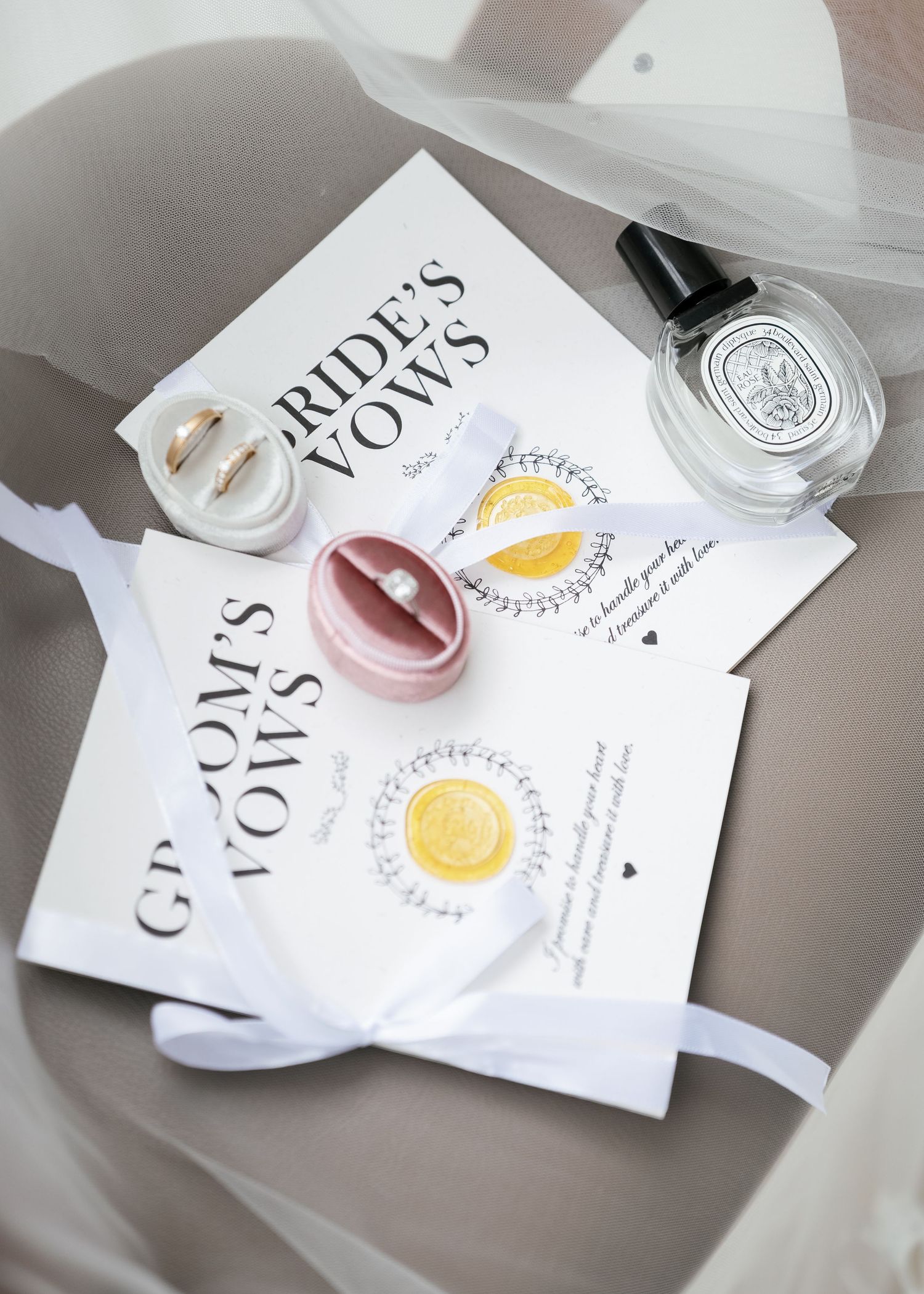 Wedding vows and invitations styled with a perfume bottle and ring boxes against a light gray fabric background.