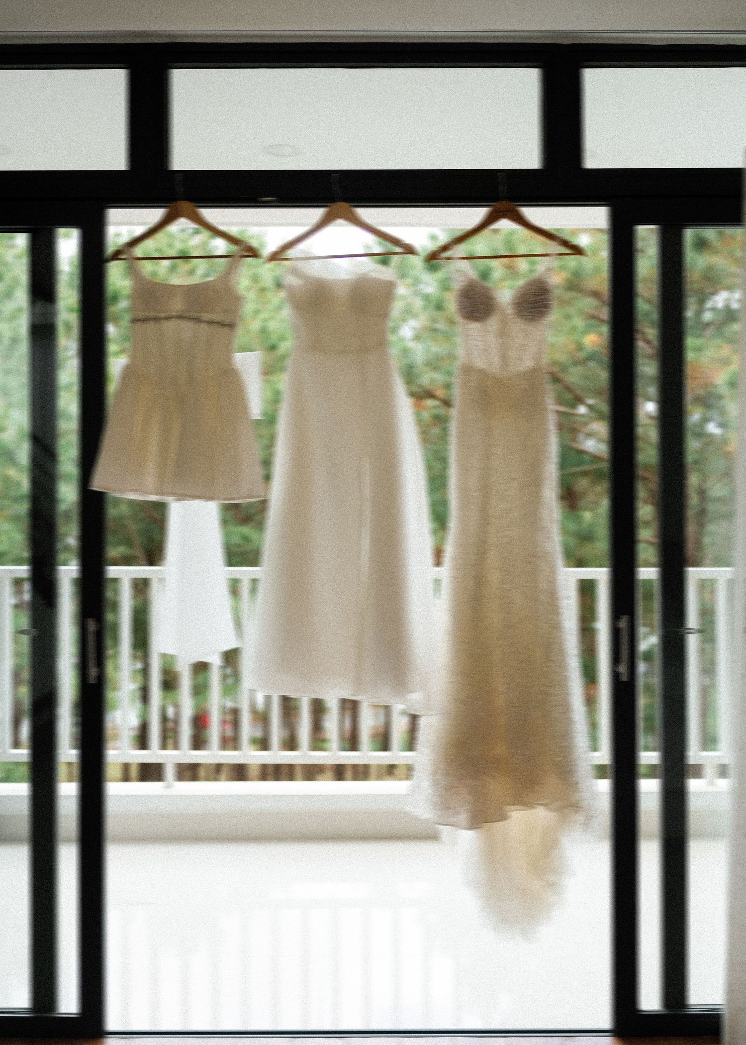 A row of elegant white and cream wedding dresses hanging from wooden hangers against a bright window.