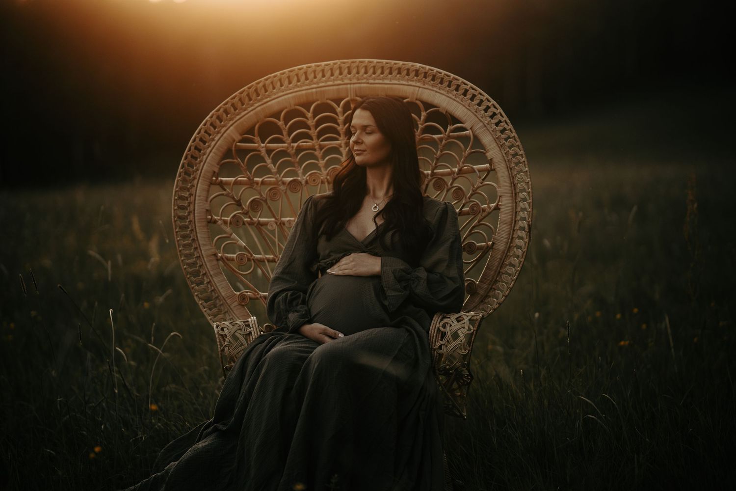 Maternity portrait featuring a wicker peacock chair in a dreamy sunset field setting.