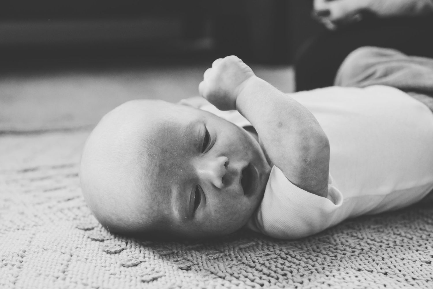 A black and white photo of an infant lying on a textured blanket.