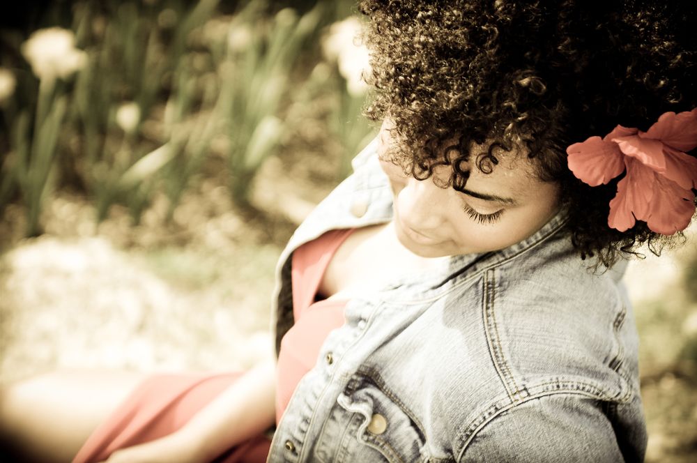 Artistic portrait with curly hair and denim jacket in soft focus with a pink flower accent.
