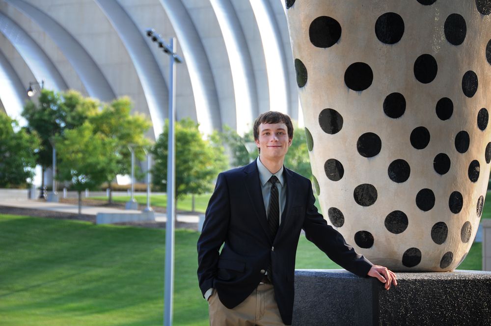 Professional standing beside large polka-dotted architectural structure outdoors on manicured lawn.