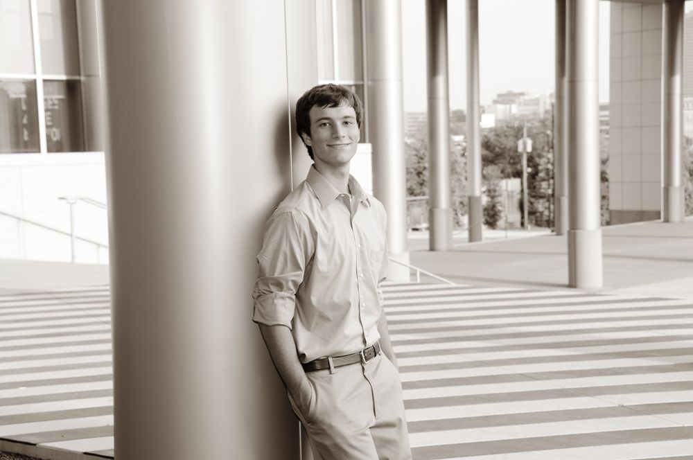 Black and white portrait showing casual attire against architectural columns and lines.
