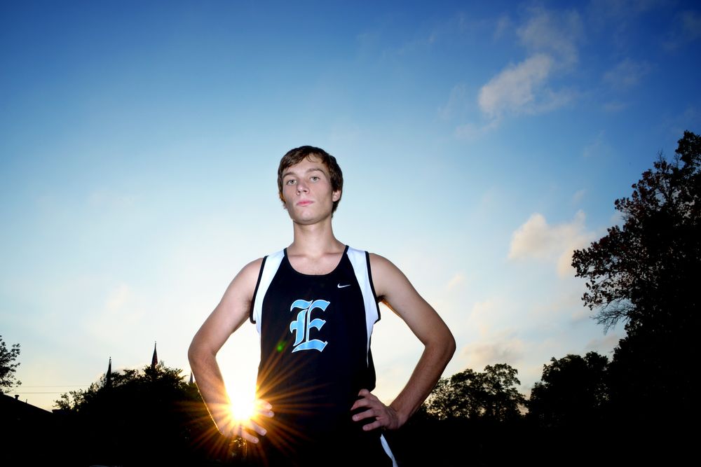 Athletic figure in track uniform silhouetted against sunset sky.